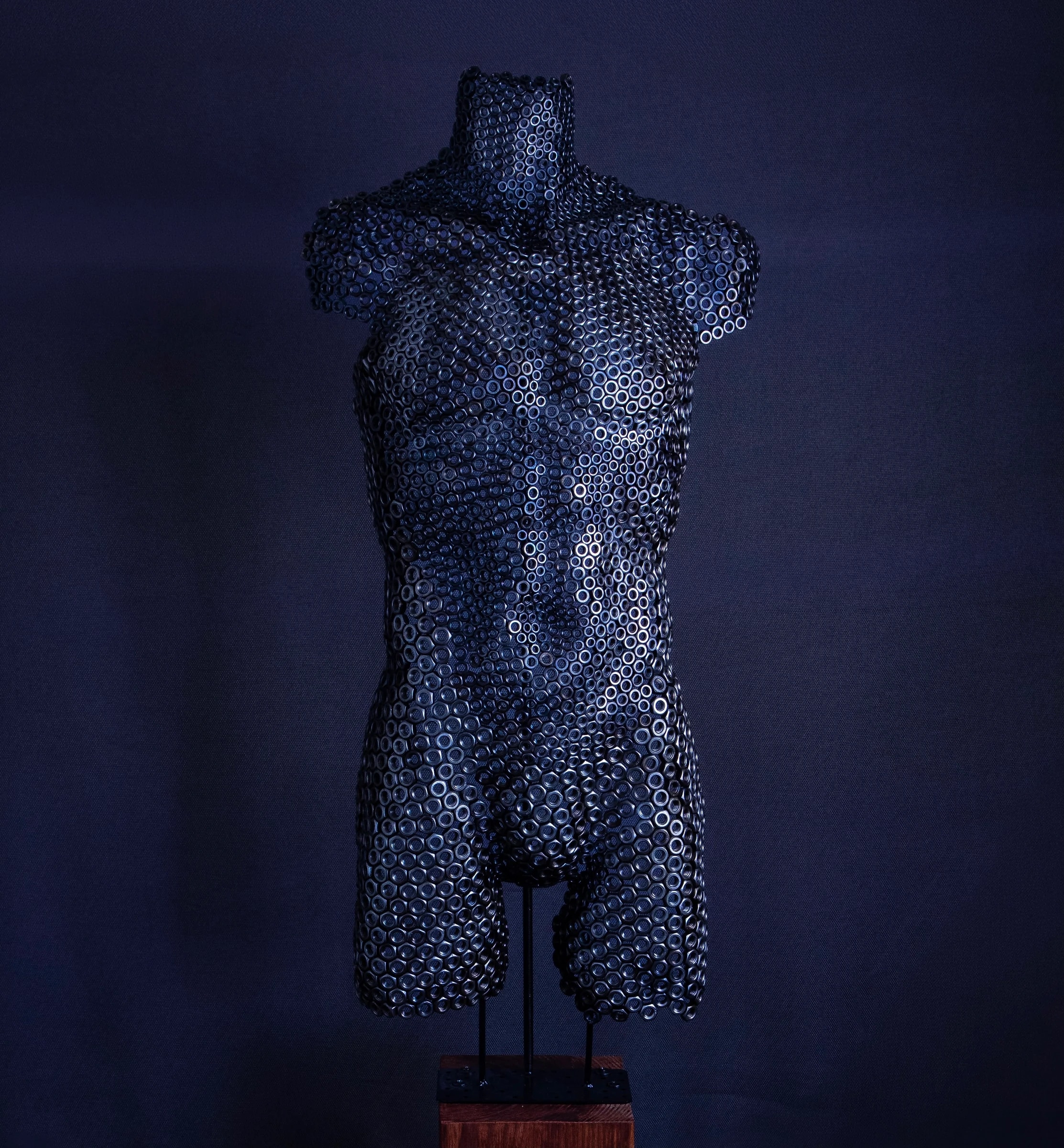Forged Identity — mannelijke torso van zwarte stalen moeren op een houten sokkel